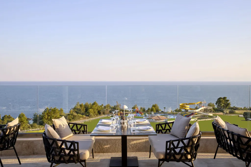Tables dressées sur une terrasse avec vue sur la mer et un parc aquatique.