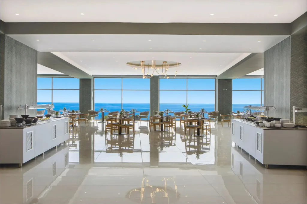 Une salle lumineuse avec des buffets et une vue sur la mer par de grandes baies vitrées.