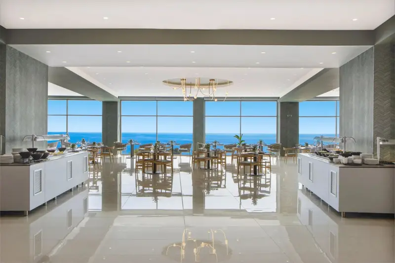 Une salle lumineuse avec des buffets et une vue sur la mer par de grandes baies vitrées.
