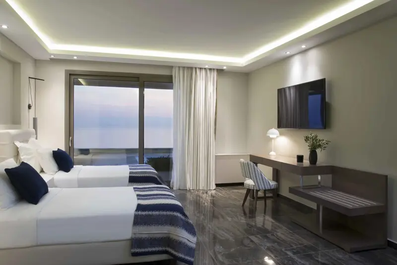 Chambre lumineuse avec deux lits et vue sur la mer.