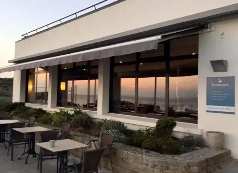 Terrasse avec tables et chaises donnant sur une vue mer au coucher du soleil.