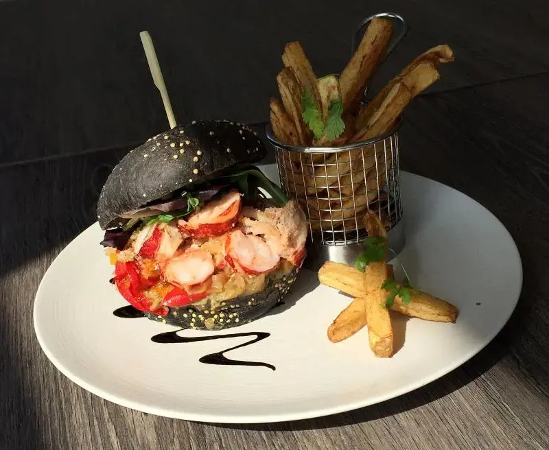 Un hamburger noir garni de fruits de mer est servi avec des frites.