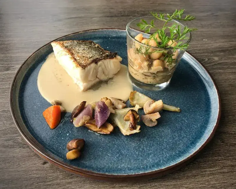 Assiette de poisson blanc avec sauce crémeuse, légumes et une verrine de salade.