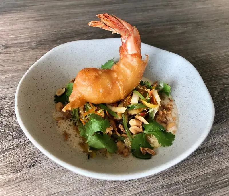 Une assiette de crevettes panées est présentée sur une table en bois.