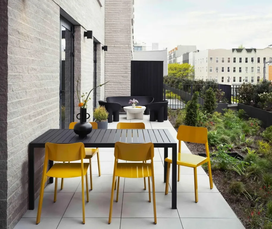 Une table et des chaises jaunes sont disposées sur une terrasse carrelée.