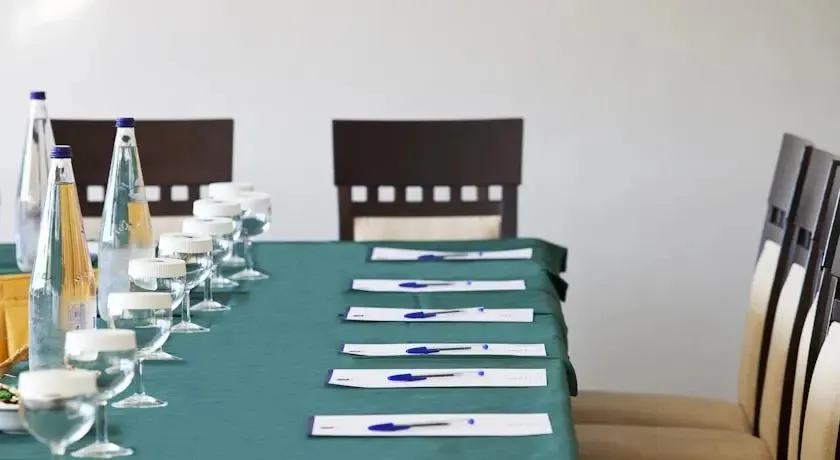 Une longue table verte est préparée pour une réunion avec des verres d'eau et des stylos.