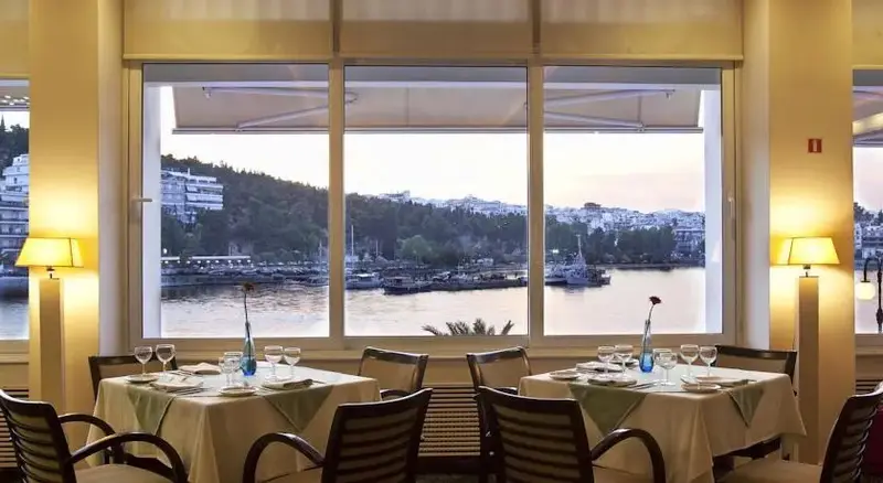 Une salle à manger lumineuse offre une vue sur un port et une colline.