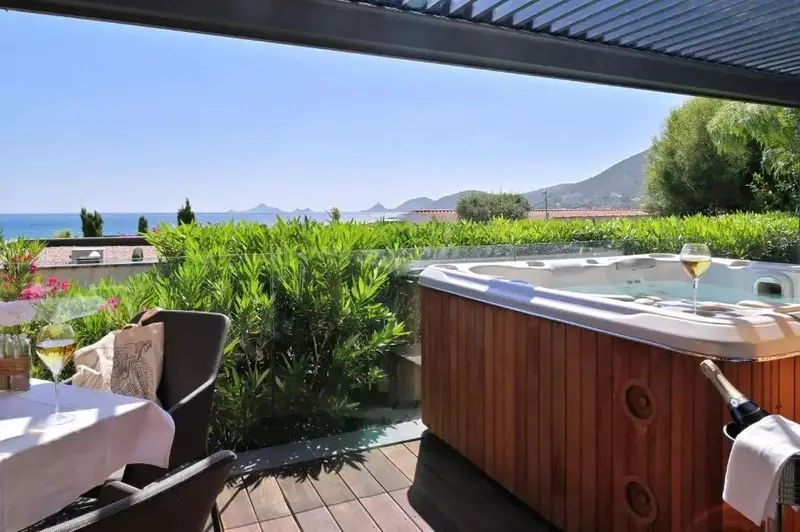 Un jacuzzi en bois sur une terrasse avec vue sur la mer et la végétation.