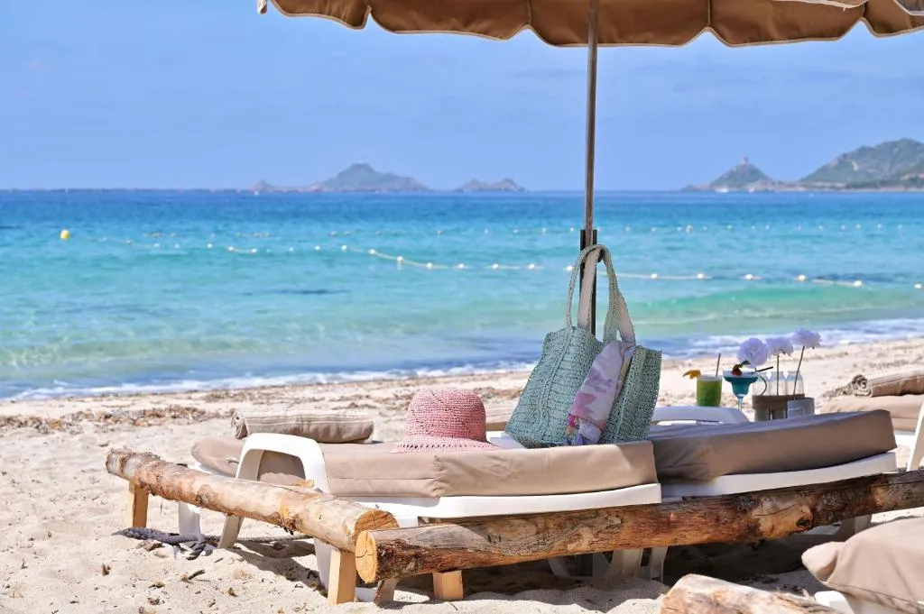 Transats et parasol sur une plage de sable fin avec vue sur la mer.
