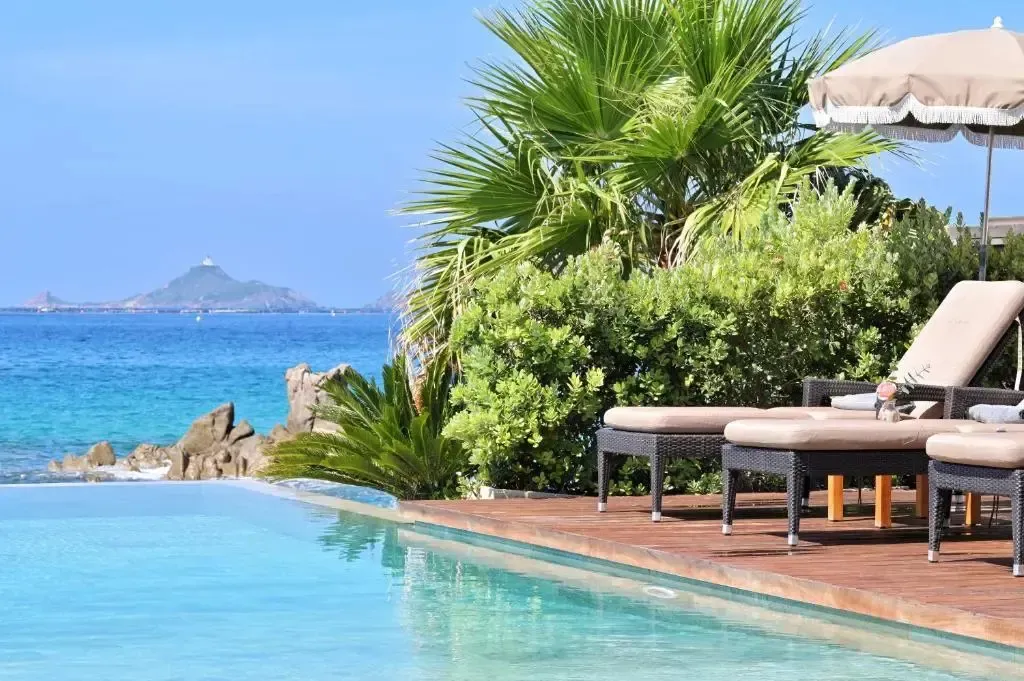 Transats et parasol au bord d'une piscine avec vue sur la mer.