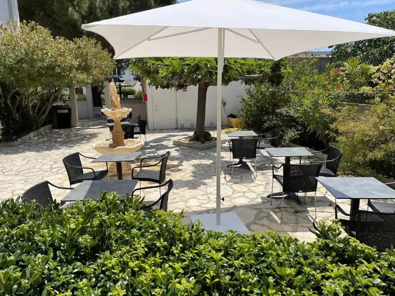 Une cour pavée avec des tables et des chaises ombragées par un parasol et des arbres.