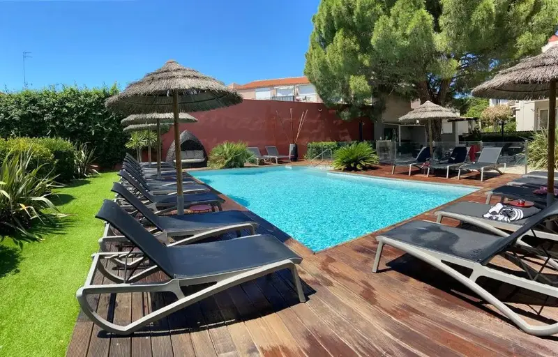 Transats et parasols ombragent une piscine rectangulaire entourée d'une terrasse en bois.
