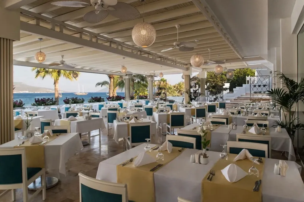 Une salle de restaurant lumineuse avec des tables dressées face à la mer.