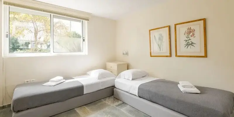 Une chambre lumineuse avec deux lits simples et des tableaux floraux.