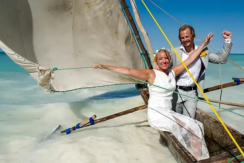 Un couple celebre un evenement a bord d'un bateau traditionnel en bois sur une plage de sable blanc.