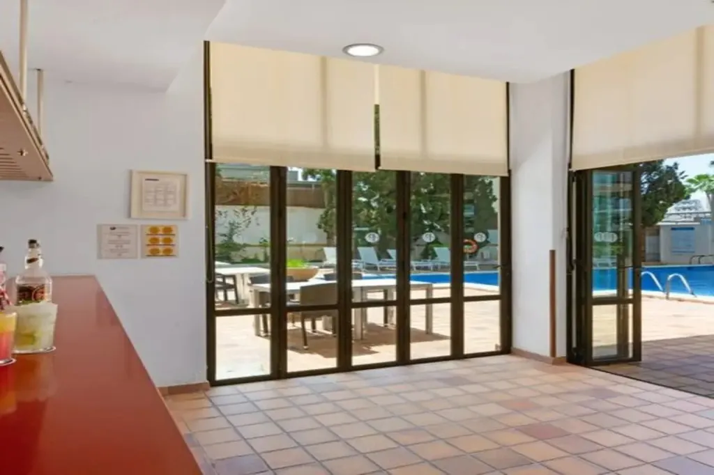 Un comptoir de bar s'ouvre sur une terrasse avec des transats près d'une piscine.