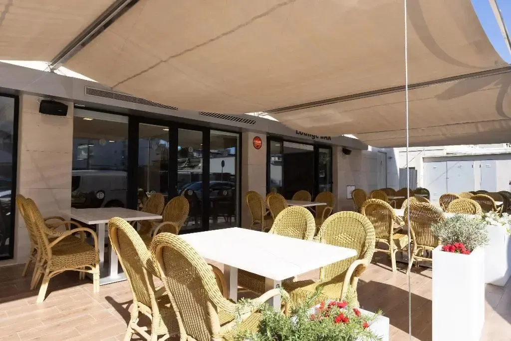 Terrasse ombragée avec tables et chaises en osier.
