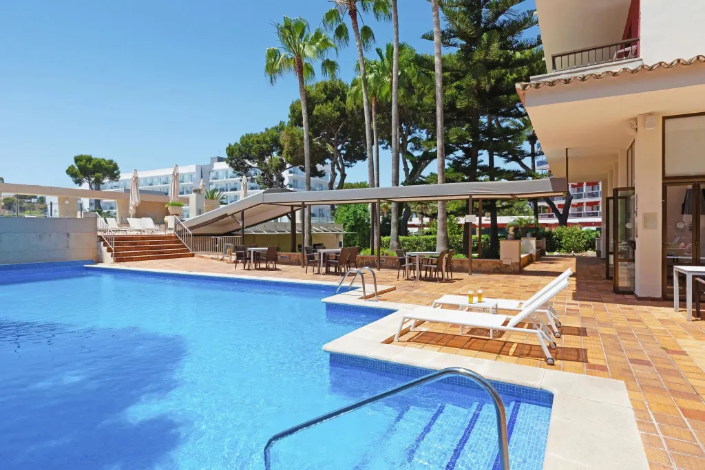 Une piscine turquoise bordée de transats et d'une terrasse ombragée.