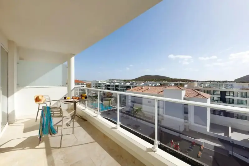 Une terrasse ensoleillée offre une vue sur un paysage urbain et des collines au loin.