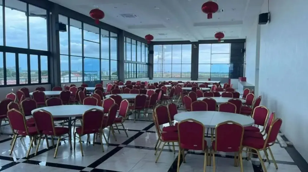 Une grande salle lumineuse avec de nombreuses tables et chaises est orientée vers une vue extérieure.