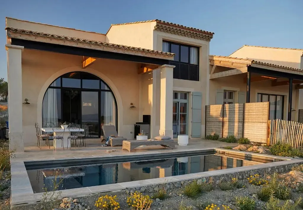 Une terrasse ombragée donne sur une petite piscine et un bâtiment aux murs clairs.