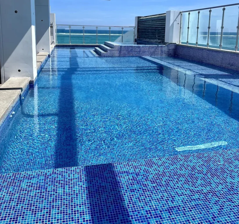 Une piscine rectangulaire bleu turquoise avec des marches et une vue sur la mer.