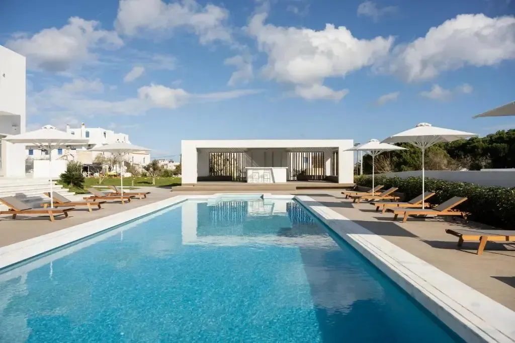 Une piscine rectangulaire bordée de transats sous des parasols blancs.