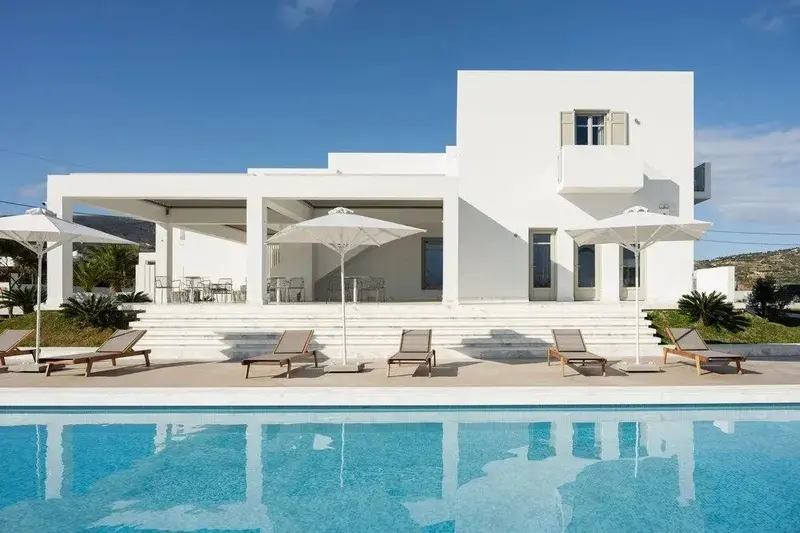 Bâtiment blanc moderne avec piscine et chaises longues sous des parasols.