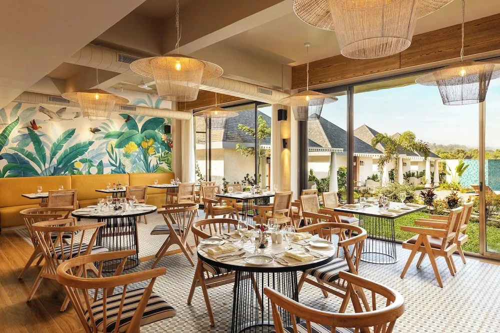 Une salle lumineuse avec des tables dressées pour un repas, donnant sur un jardin tropical.