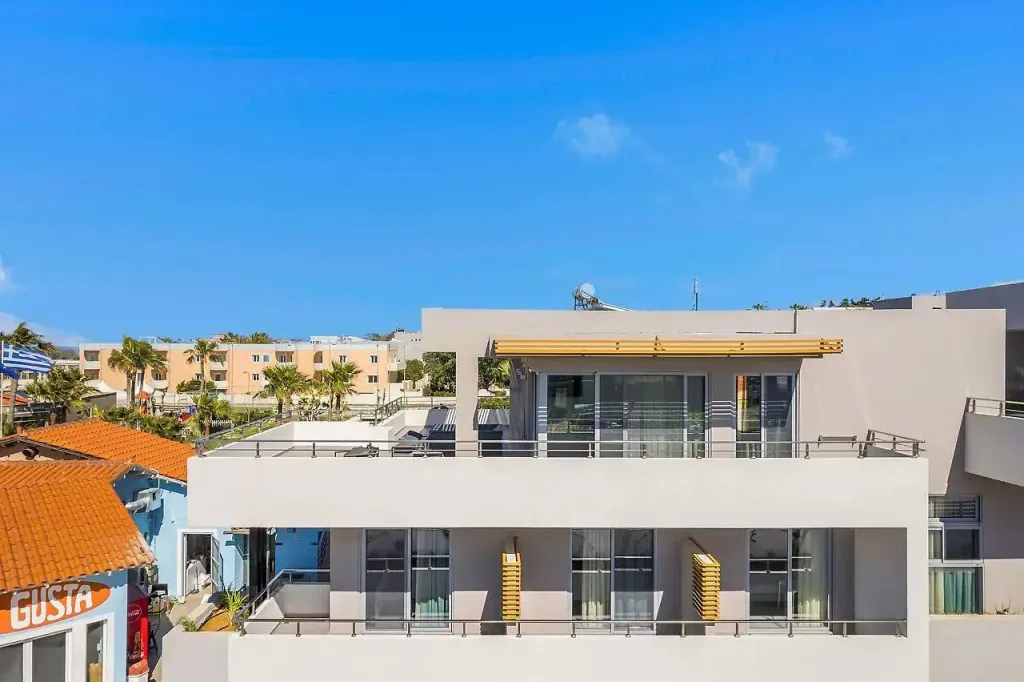 Bâtiment moderne avec des balcons et des terrasses ensoleillés, surplombant un paysage urbain.