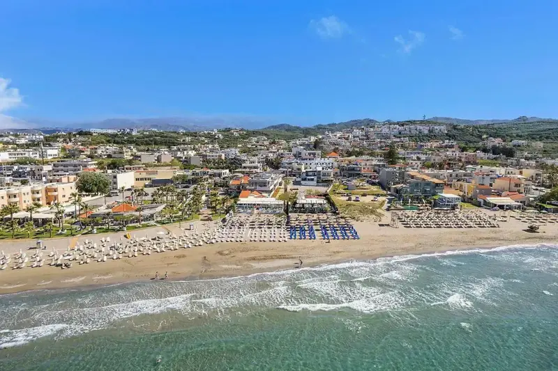 Vue aérienne d'une plage ensoleillée bordée de transats et d'une station balnéaire.