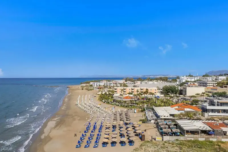 Vue aérienne d'une plage ensoleillée avec des transats et des parasols alignés le long du rivage.