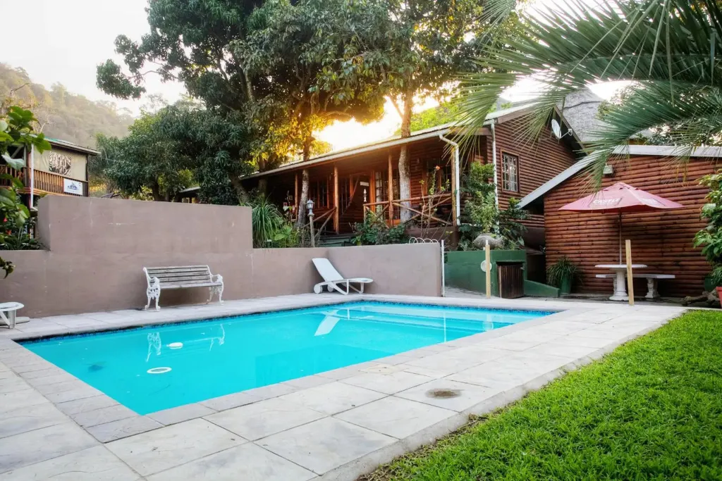 Une piscine rectangulaire bordée d'une terrasse ensoleillée et de végétation luxuriante.