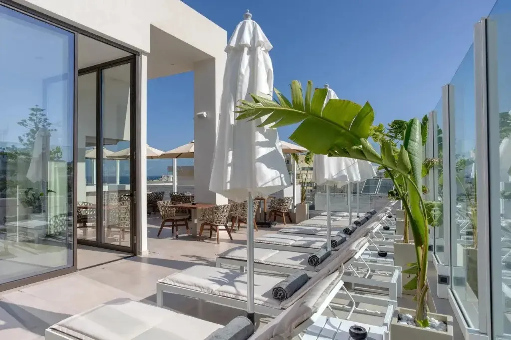 Terrasse aménagée avec transats et parasols blancs, offrant une vue sur la mer.