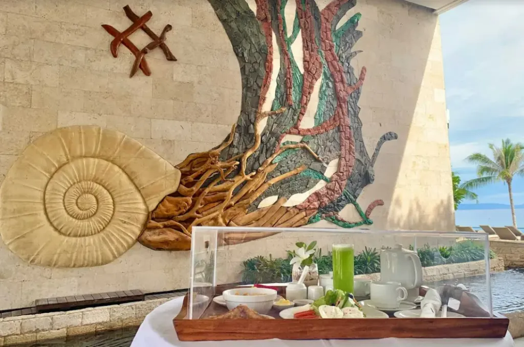 Un plateau de petit-déjeuner est présenté devant un mur décoré d'un motif de coquillage et d'arbres.
