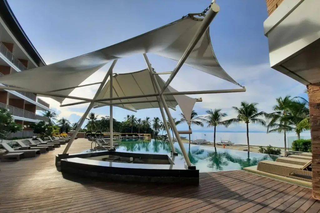 Terrasse ombragée avec piscine et vue sur la mer.