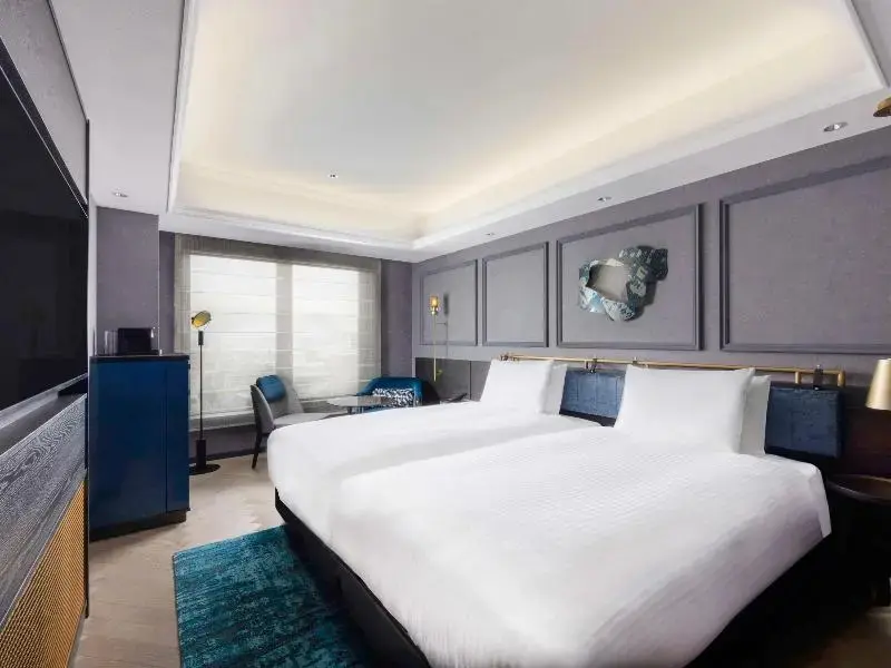 Une chambre lumineuse avec un grand lit et un coin salon près de la fenêtre.