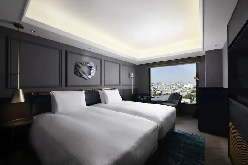 Chambre moderne avec deux lits simples et une grande fenêtre offrant une vue sur la ville.