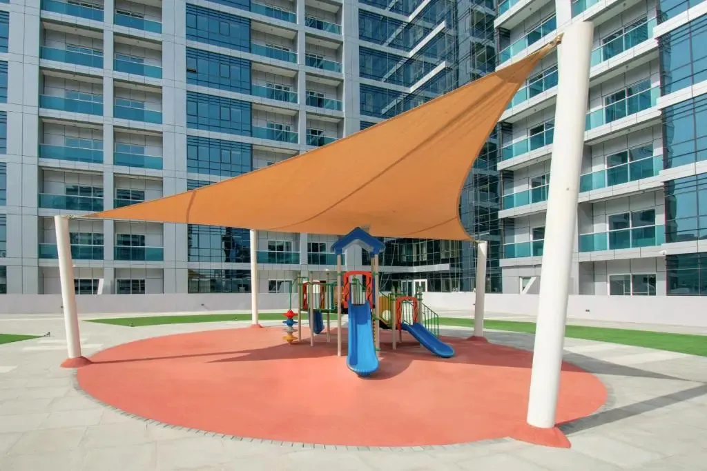 Espace de jeux pour enfants ombragé avec toboggan et sol souple.
