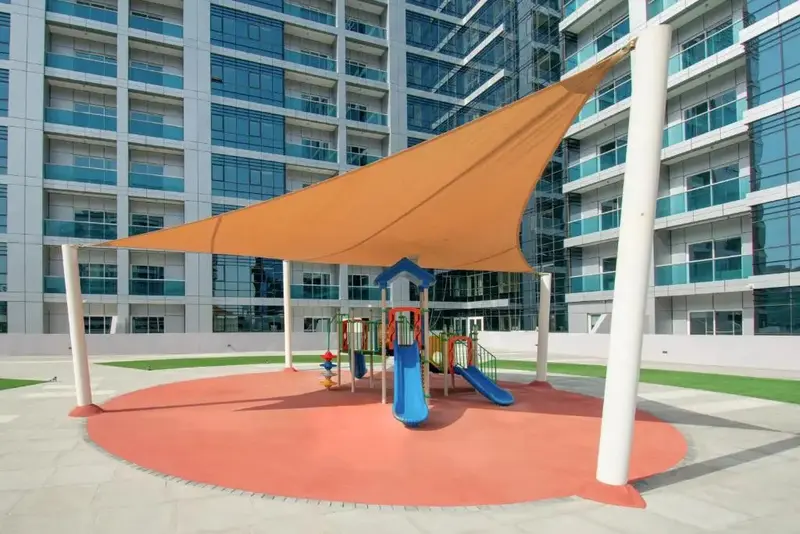 Espace de jeux pour enfants ombragé avec toboggan et sol souple.
