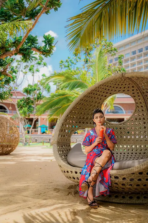 Une femme assise dans un fauteuil en osier sur une plage de sable.