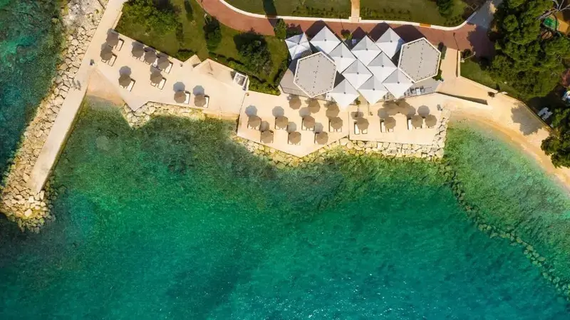 Vue aérienne d'une plage avec des parasols et des bâtiments blancs.