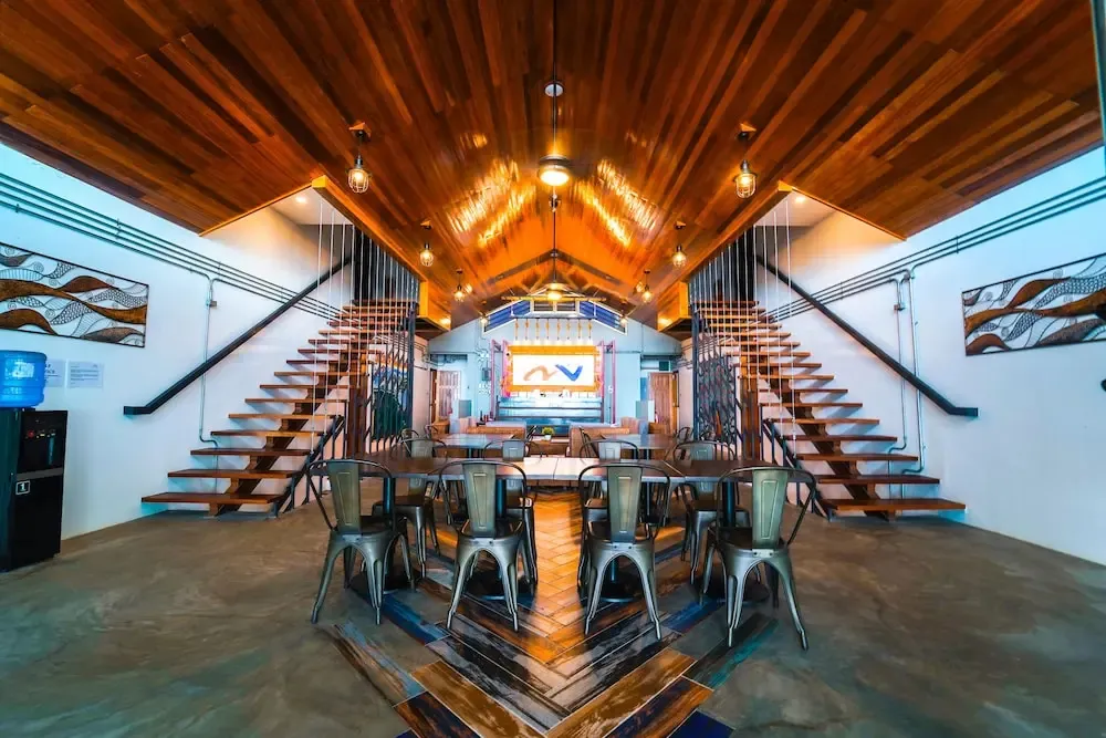 Une grande salle à manger avec des tables en bois et des escaliers menant à une mezzanine.