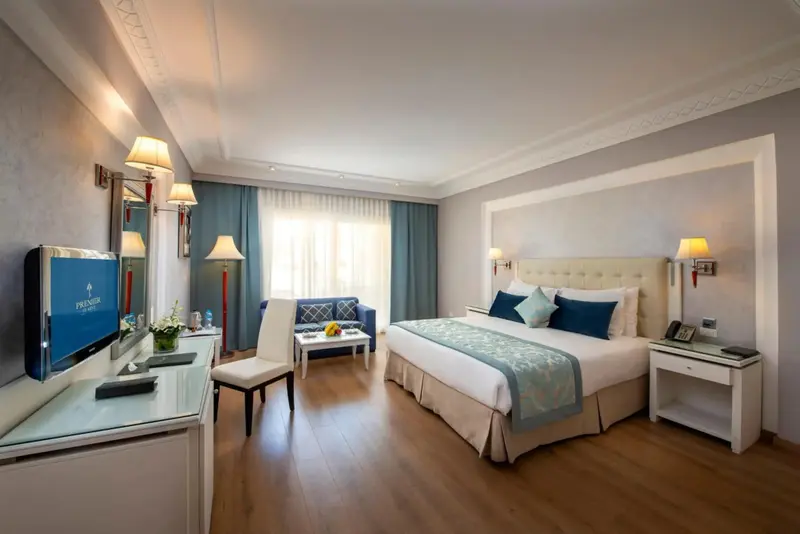 Une chambre lumineuse avec un grand lit et un coin salon près de la fenêtre.