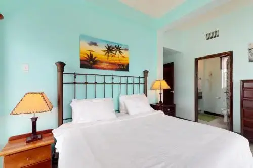 Une chambre lumineuse avec un lit recouvert d'une courtepointe blanche et une décoration murale tropicale.