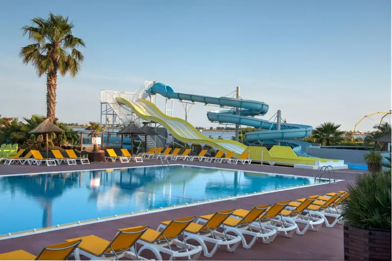 Une piscine avec des transats et des toboggans aquatiques sous le soleil.