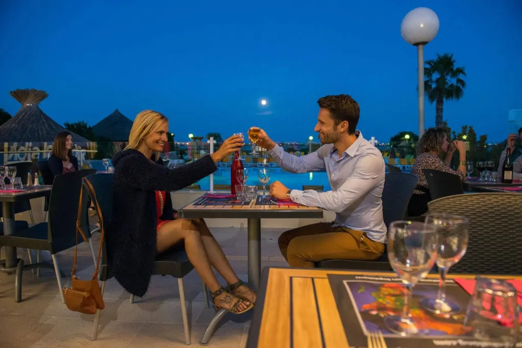 Un couple trinque avec des verres de vin à une table en terrasse.