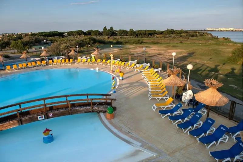 Transats et parasols bordent une piscine rectangulaire aux eaux turquoise.