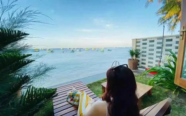 Une personne est assise sur une terrasse en bois face à la mer.