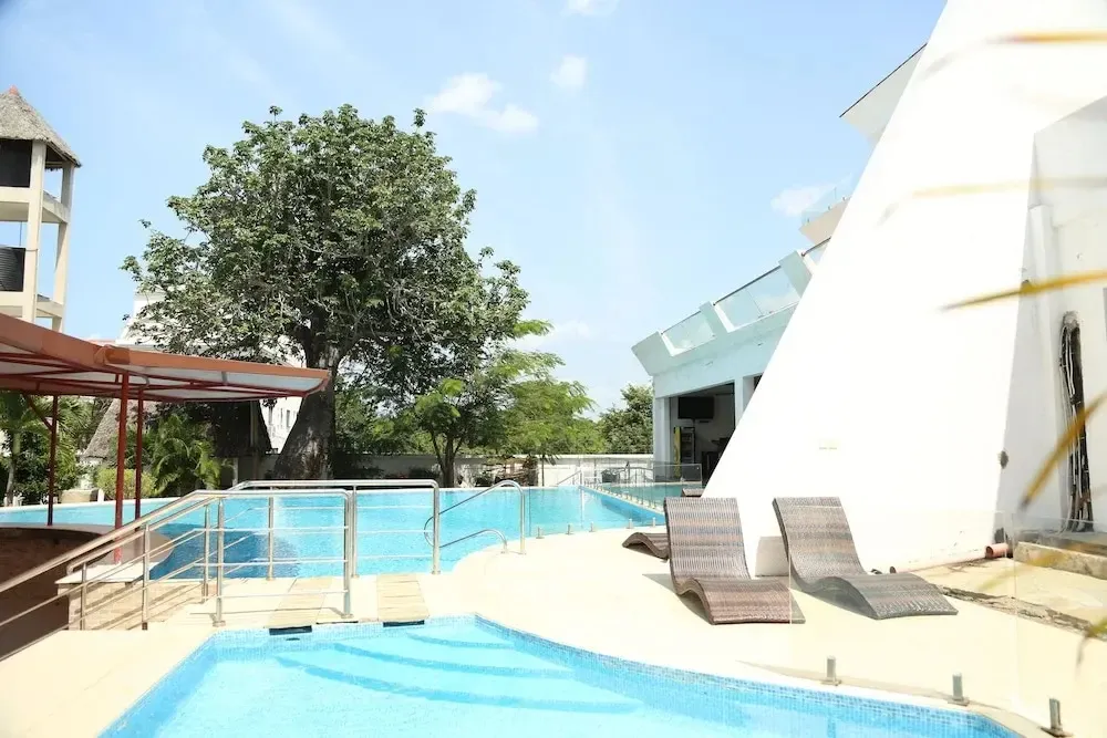 Piscine bleue avec transats et végétation luxuriante en arrière-plan.